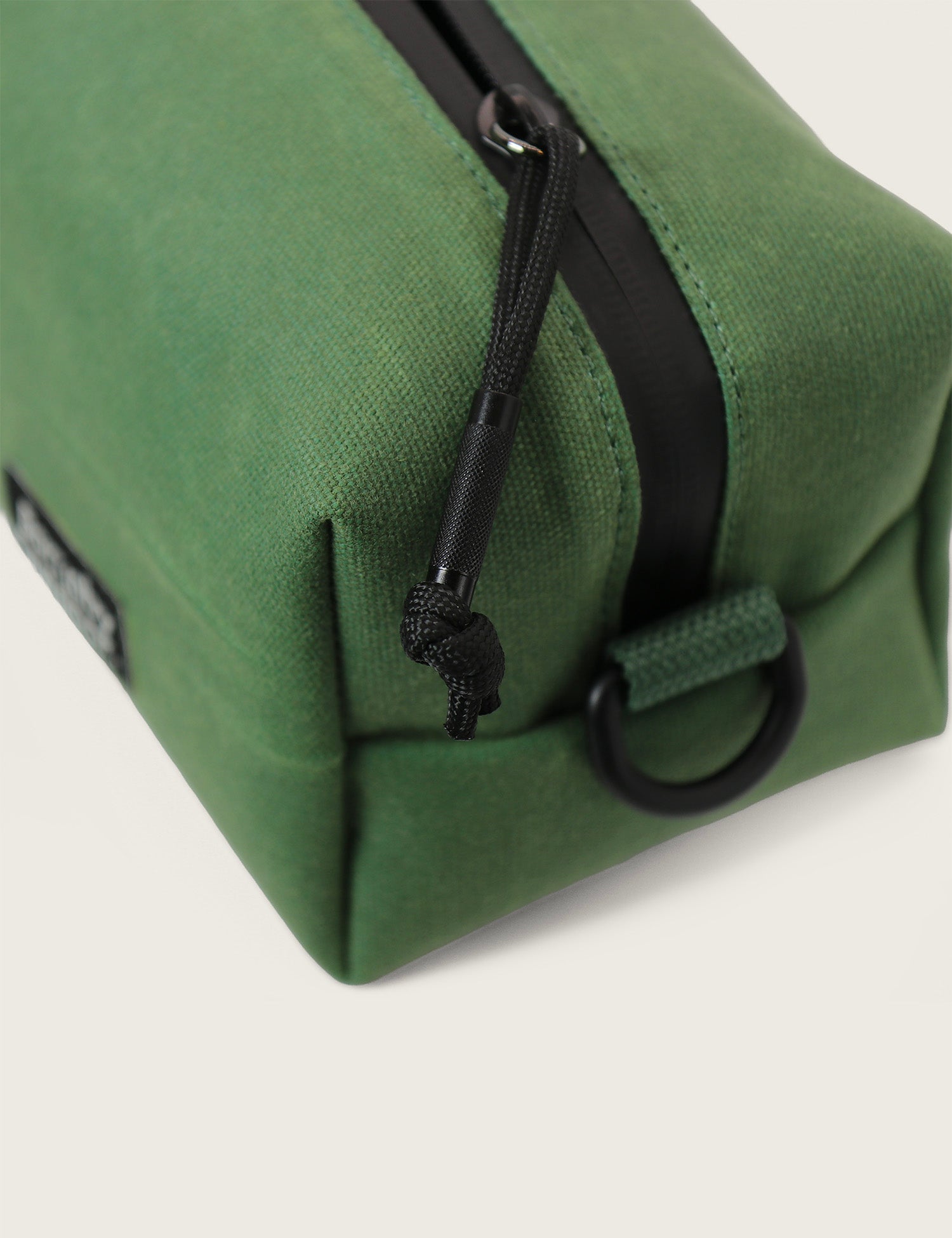 Green toiletry bag with black zipper and strap on a light gray background