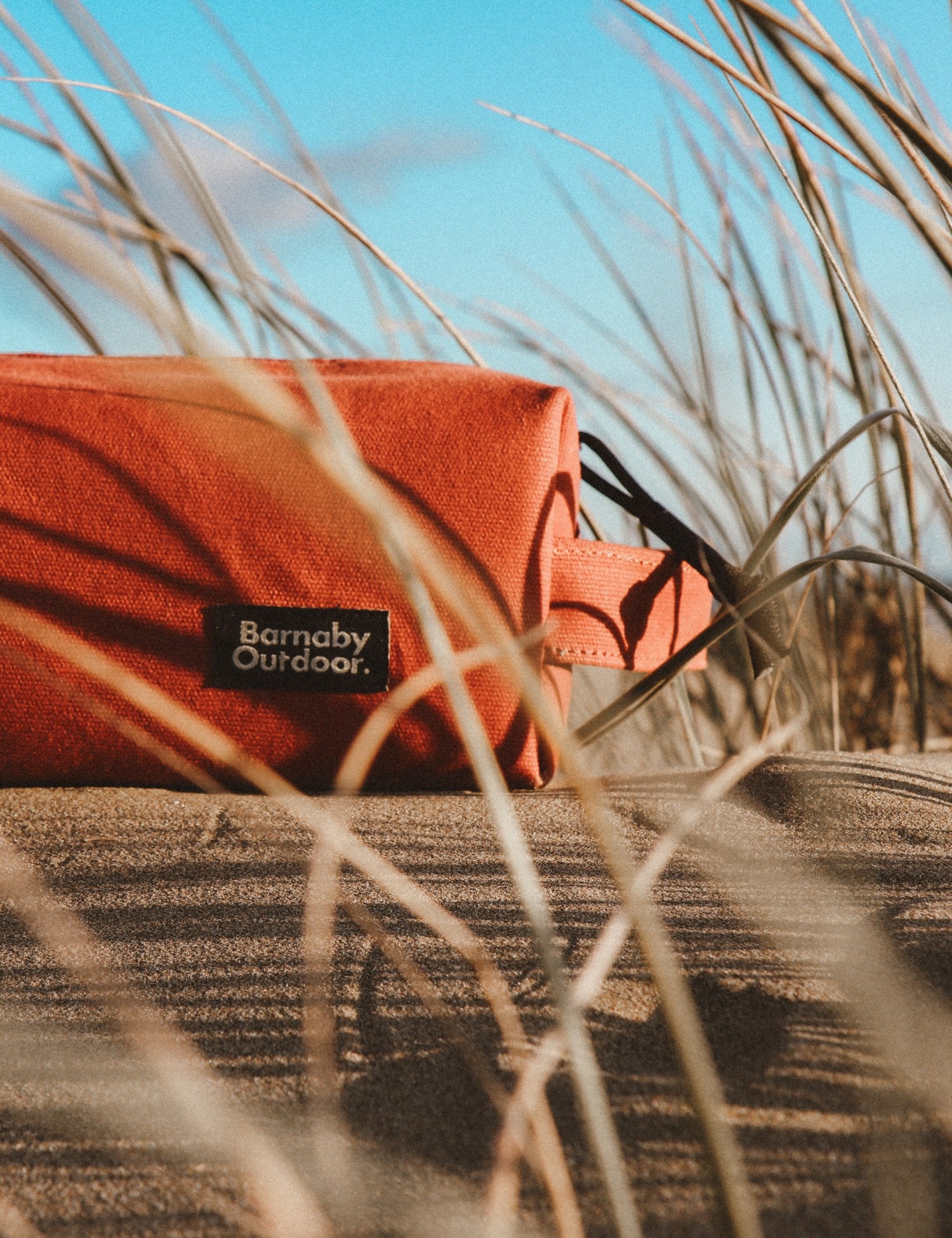 Orange pouch with 'Barnaby Outdoor' logo on sand and grass
