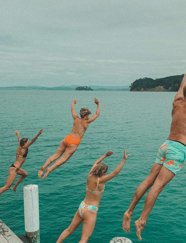 Four people jumping into a body of water from a dock.