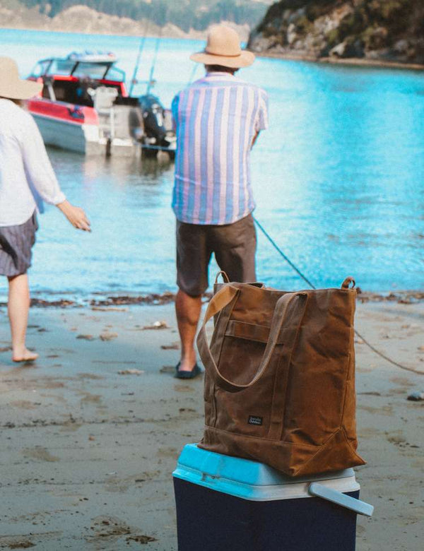 Man pulling bote in on a beach with a tussock brown Barnaby better tote and cooler in the foreground