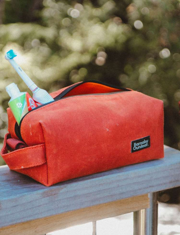 Tongariro red Field wash bag or toiletry bag with travel items on a wooden surface outdoors