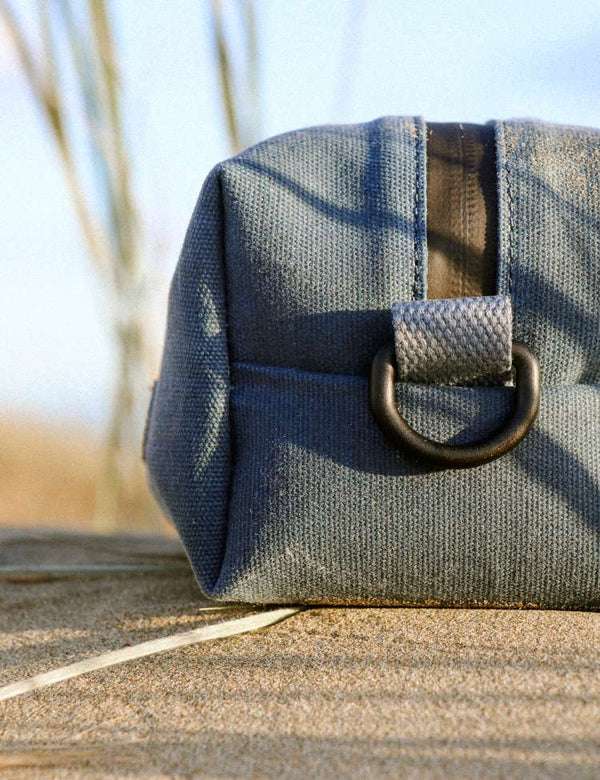Blue Canvas wash bag with a aluminium buckle on a sandy surface