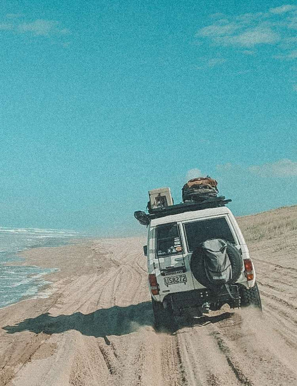 4x4 vehicle on a sandy beach with ocean and sky in the background