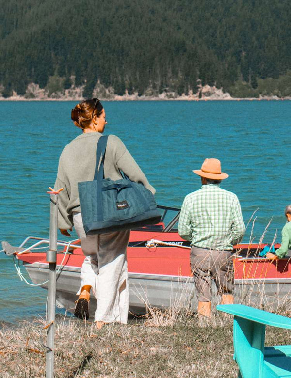 Two people with a boat on a lake, one person carrying a blue barnaby outdoor bag.