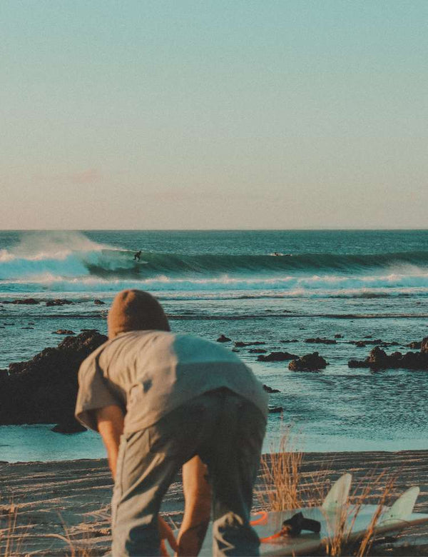 Person standing on a beach with surfboards, looking out at the ocean.