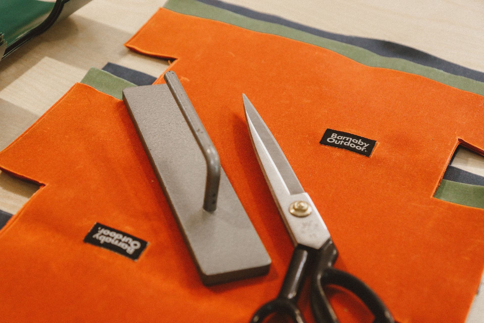 Scissors and a pattern weight tool sitting on waxed canvas fabric with a brand label.