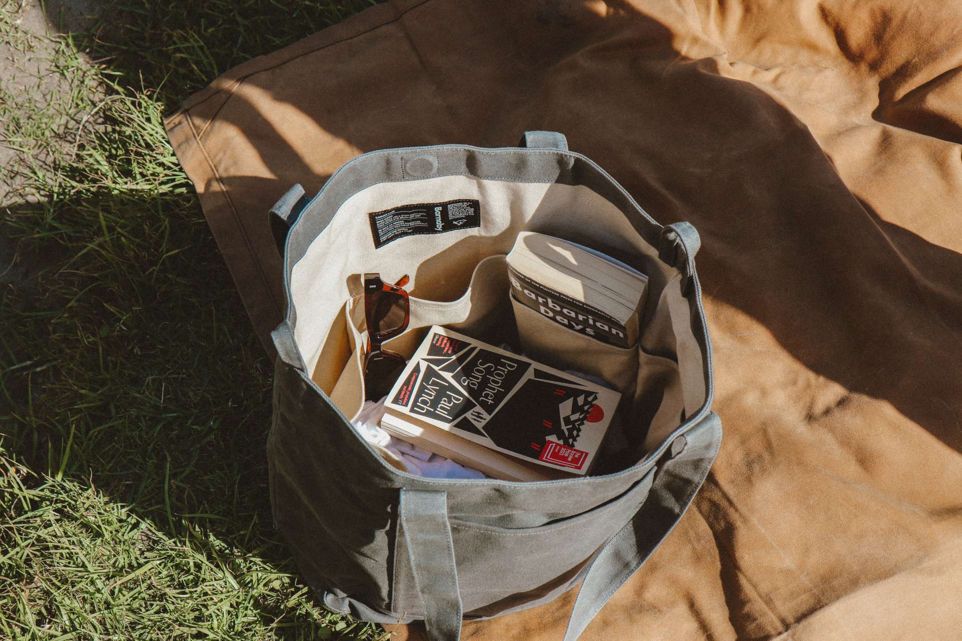Gray Waxed camnvas tote bag with snacks on a brown canvas mat outdoors